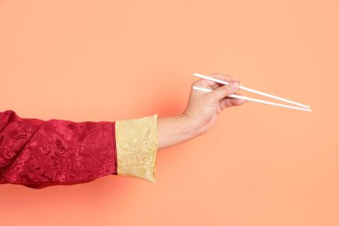 Yeni Çin yılın kutlu olsun. Kırmızı geleneksel cheongsam qipao ya da changshan elbisesi giyen Asyalı son sınıf öğrencisinin eli turuncu arka planda izole edilmiş beyaz çubuklarla el ele tutuşuyor..