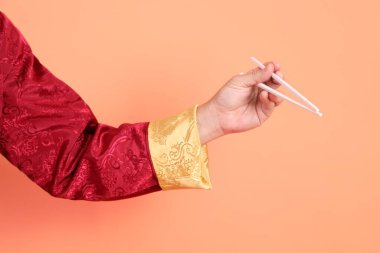 Yeni Çin yılın kutlu olsun. Kırmızı geleneksel cheongsam qipao ya da changshan elbisesi giyen Asyalı son sınıf öğrencisinin eli turuncu arka planda izole edilmiş beyaz çubuklarla el ele tutuşuyor..