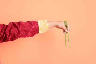 Yeni Çin yılın kutlu olsun. Kırmızı geleneksel cheongsam qipao ya da changshan elbisesi giyen Asyalı son sınıf öğrencisinin eli turuncu arka planda izole edilmiş yeşil çubuklarla el ele tutuşuyor..