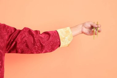 Yeni Çin yılın kutlu olsun. Kırmızı geleneksel cheongsam qipao ya da changshan elbisesi giyen Asyalı son sınıf öğrencisinin eli turuncu arka planda izole edilmiş yeşil çubuklarla el ele tutuşuyor..