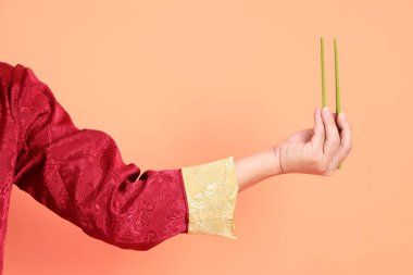 Yeni Çin yılın kutlu olsun. Kırmızı geleneksel cheongsam qipao ya da changshan elbisesi giyen Asyalı son sınıf öğrencisinin eli turuncu arka planda izole edilmiş yeşil çubuklarla el ele tutuşuyor..