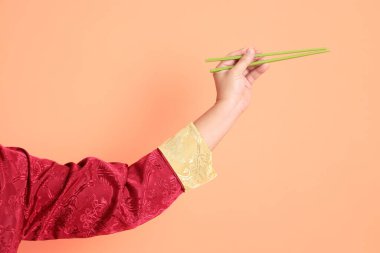 Yeni Çin yılın kutlu olsun. Kırmızı geleneksel cheongsam qipao ya da changshan elbisesi giyen Asyalı son sınıf öğrencisinin eli turuncu arka planda izole edilmiş yeşil çubuklarla el ele tutuşuyor..