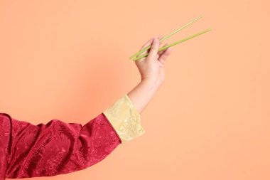 Yeni Çin yılın kutlu olsun. Kırmızı geleneksel cheongsam qipao ya da changshan elbisesi giyen Asyalı son sınıf öğrencisinin eli turuncu arka planda izole edilmiş yeşil çubuklarla el ele tutuşuyor..