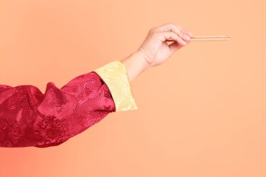 Yeni Çin yılın kutlu olsun. Kırmızı geleneksel cheongsam qipao ya da changshan elbisesi giyen Asyalı son sınıf öğrencisinin eli. Turuncu arka planda izole edilmiş ahşap çubukları tutan el hareketi..