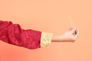 Yeni Çin yılın kutlu olsun. Kırmızı geleneksel cheongsam qipao ya da changshan elbisesi giyen Asyalı son sınıf öğrencisinin eli. Turuncu arka planda izole edilmiş ahşap çubukları tutan el hareketi..