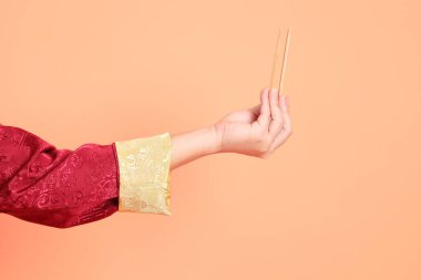 Yeni Çin yılın kutlu olsun. Kırmızı geleneksel cheongsam qipao ya da changshan elbisesi giyen Asyalı son sınıf öğrencisinin eli. Turuncu arka planda izole edilmiş ahşap çubukları tutan el hareketi..