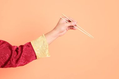 Yeni Çin yılın kutlu olsun. Kırmızı geleneksel cheongsam qipao ya da changshan elbisesi giyen Asyalı son sınıf öğrencisinin eli. Turuncu arka planda izole edilmiş ahşap çubukları tutan el hareketi..