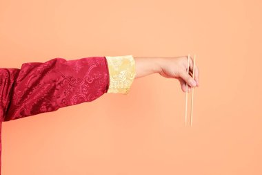 Yeni Çin yılın kutlu olsun. Kırmızı geleneksel cheongsam qipao ya da changshan elbisesi giyen Asyalı son sınıf öğrencisinin eli. Turuncu arka planda izole edilmiş ahşap çubukları tutan el hareketi..