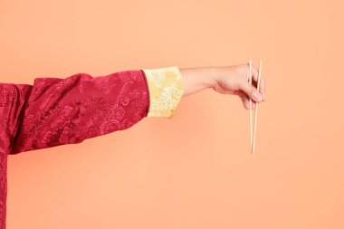 Yeni Çin yılın kutlu olsun. Kırmızı geleneksel cheongsam qipao ya da changshan elbisesi giyen Asyalı son sınıf öğrencisinin eli. Turuncu arka planda izole edilmiş ahşap çubukları tutan el hareketi..