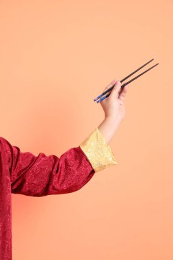 Yeni Çin yılın kutlu olsun. Kırmızı geleneksel Cheongsam Qipao ya da Changshan elbisesi giyen Asyalı son sınıf öğrencisinin eli. Çin usulü yemek çubukları turuncu arka planda izole edilmiş..