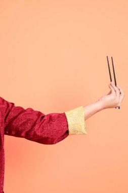 Yeni Çin yılın kutlu olsun. Kırmızı geleneksel Cheongsam Qipao ya da Changshan elbisesi giyen Asyalı son sınıf öğrencisinin eli. Çin usulü yemek çubukları turuncu arka planda izole edilmiş..
