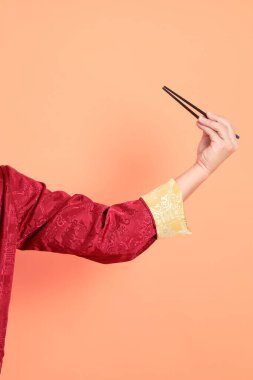 Yeni Çin yılın kutlu olsun. Kırmızı geleneksel Cheongsam Qipao ya da Changshan elbisesi giyen Asyalı son sınıf öğrencisinin eli. Çin usulü yemek çubukları turuncu arka planda izole edilmiş..