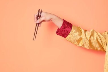 Yeni Çin yılın kutlu olsun. Asya 'lı son sınıf öğrencisi altın rengi Cheongsam Qipao ya da Changshan elbisesi giyiyor ve kahverengi çubukları turuncu arka planda tutuyor..