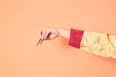 Yeni Çin yılın kutlu olsun. Asya 'lı son sınıf öğrencisi altın rengi Cheongsam Qipao ya da Changshan elbisesi giyiyor ve kahverengi çubukları turuncu arka planda tutuyor..