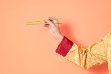 Yeni Çin yılın kutlu olsun. Asya 'lı son sınıf öğrencisi altın rengi Cheongsam Qipao ya da Changshan elbisesi giyiyor ve yeşil çubukları turuncu arka planda tutuyor..