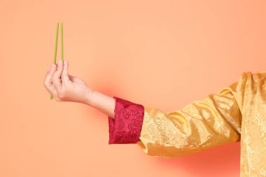 Yeni Çin yılın kutlu olsun. Asya 'lı son sınıf öğrencisi altın rengi Cheongsam Qipao ya da Changshan elbisesi giyiyor ve yeşil çubukları turuncu arka planda tutuyor..