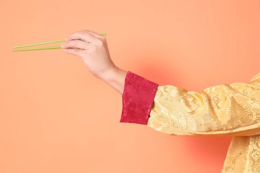 Yeni Çin yılın kutlu olsun. Asya 'lı son sınıf öğrencisi altın rengi Cheongsam Qipao ya da Changshan elbisesi giyiyor ve yeşil çubukları turuncu arka planda tutuyor..