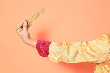 Yeni Çin yılın kutlu olsun. Asya 'lı son sınıf öğrencisi altın rengi Cheongsam Qipao ya da Changshan elbisesi giyiyor ve yeşil çubukları turuncu arka planda tutuyor..