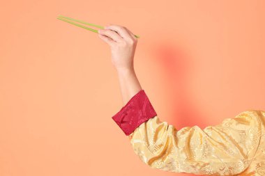 Yeni Çin yılın kutlu olsun. Asya 'lı son sınıf öğrencisi altın rengi Cheongsam Qipao ya da Changshan elbisesi giyiyor ve yeşil çubukları turuncu arka planda tutuyor..