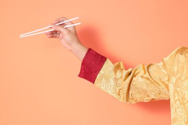 Yeni Çin yılın kutlu olsun. Asya 'lı son sınıf öğrencisi altın rengi Cheongsam Qipao ya da Changshan elbisesi giyiyor. El hareketleriyle turuncu arka planda beyaz çubukları tutuyor..