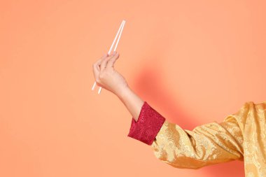 Yeni Çin yılın kutlu olsun. Asya 'lı son sınıf öğrencisi altın rengi Cheongsam Qipao ya da Changshan elbisesi giyiyor. El hareketleriyle turuncu arka planda beyaz çubukları tutuyor..