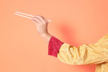 Yeni Çin yılın kutlu olsun. Asya 'lı son sınıf öğrencisi altın rengi Cheongsam Qipao ya da Changshan elbisesi giyiyor. El hareketleriyle turuncu arka planda beyaz çubukları tutuyor..