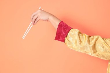 Yeni Çin yılın kutlu olsun. Asya 'lı son sınıf öğrencisi altın rengi Cheongsam Qipao ya da Changshan elbisesi giyiyor. El hareketleriyle turuncu arka planda beyaz çubukları tutuyor..