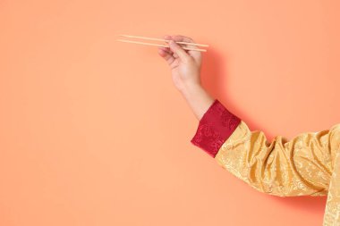 Yeni Çin yılın kutlu olsun. Asya 'lı son sınıf öğrencisi altın rengi Cheongsam Qipao ya da Changshan elbisesi giyiyor. Elleri ahşap çubukları turuncu arka planda tutuyor..