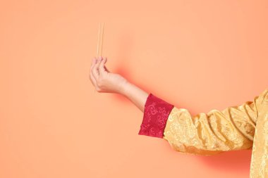 Yeni Çin yılın kutlu olsun. Asya 'lı son sınıf öğrencisi altın rengi Cheongsam Qipao ya da Changshan elbisesi giyiyor. Elleri ahşap çubukları turuncu arka planda tutuyor..