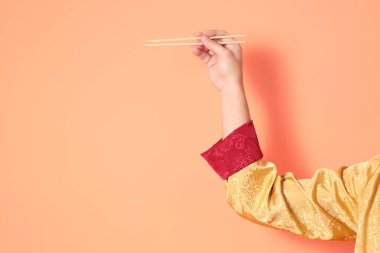 Yeni Çin yılın kutlu olsun. Asya 'lı son sınıf öğrencisi altın rengi Cheongsam Qipao ya da Changshan elbisesi giyiyor. Elleri ahşap çubukları turuncu arka planda tutuyor..