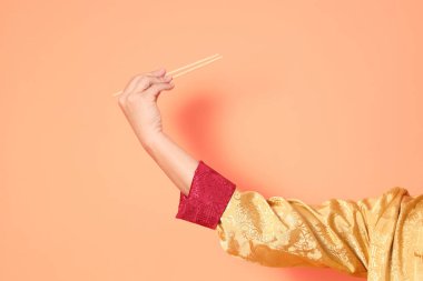 Yeni Çin yılın kutlu olsun. Asya 'lı son sınıf öğrencisi altın rengi Cheongsam Qipao ya da Changshan elbisesi giyiyor. Elleri ahşap çubukları turuncu arka planda tutuyor..