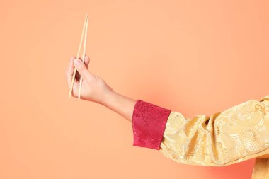 Yeni Çin yılın kutlu olsun. Asya 'lı son sınıf öğrencisi altın rengi Cheongsam Qipao ya da Changshan elbisesi giyiyor. Elleri ahşap çubukları turuncu arka planda tutuyor..