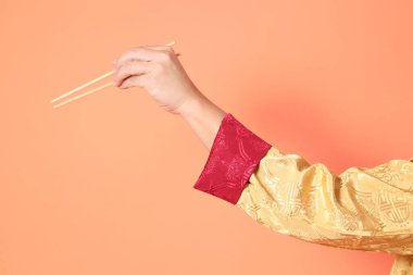 Yeni Çin yılın kutlu olsun. Asya 'lı son sınıf öğrencisi altın rengi Cheongsam Qipao ya da Changshan elbisesi giyiyor. Elleri ahşap çubukları turuncu arka planda tutuyor..