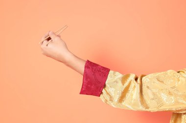 Yeni Çin yılın kutlu olsun. Asya 'lı son sınıf öğrencisi altın rengi Cheongsam Qipao ya da Changshan elbisesi giyiyor. Elleri ahşap çubukları turuncu arka planda tutuyor..