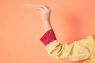 Yeni Çin yılın kutlu olsun. Asya 'lı son sınıf öğrencisi altın rengi Cheongsam Qipao ya da Changshan elbisesi giyiyor. Elleri ahşap çubukları turuncu arka planda tutuyor..