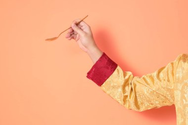 Yeni Çin yılın kutlu olsun. Asya 'lı son sınıf öğrencileri, geleneksel altın kıyafetler giyip turuncu arka planda altın kaşıkla el ele tutuşuyorlar..