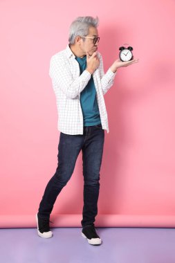 Asyalı enerjik kıdemli adam günlük kıyafetler giyiyor. Pembe arka plan, zaman yönetimi, denge...