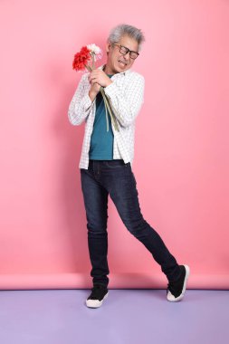Pembe arka planda izole edilmiş bir çiçek buketi tutan sıradan giyinmiş Asyalı son sınıf öğrencisi. Sevgililer Günü, Kadınlar Günü, Doğum Günü