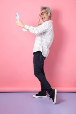 Pembe arka planda izole edilmiş cep telefonu jesti ile Asyalı son sınıf öğrencisi. Sevgililer Günü