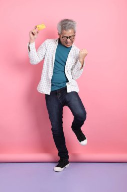 Pembe arka planda izole edilmiş kredi kartı jesti olan son sınıf Asyalı bir adam. Sevgililer Günü