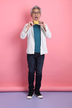 Pembe arka planda izole edilmiş kredi kartı jesti olan son sınıf Asyalı bir adam. Sevgililer Günü