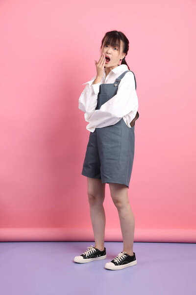Cheerful lovely young asian woman in overalls casual clothes with gesture of surprise isolated on pink background. St Valentine's Day, Women's Day, Birthday