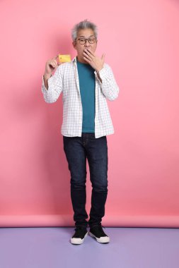 Pembe arka planda izole edilmiş kredi kartı jesti olan son sınıf Asyalı bir adam. Sevgililer Günü