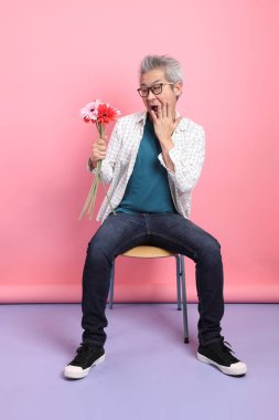 Pembe arka planda izole bir çiçek buketi tutarken sandalyede oturma jesti yapan Asyalı son sınıf öğrencisi. Sevgililer Günü
