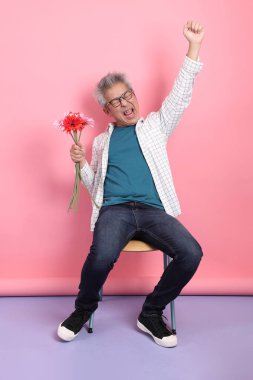 Pembe arka planda izole bir çiçek buketi tutarken sandalyede oturma jesti yapan Asyalı son sınıf öğrencisi. Sevgililer Günü