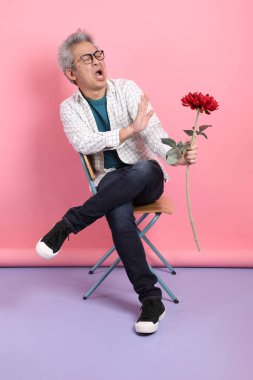 Pembe arka planda izole bir çiçek buketi tutarken sandalyede oturma jesti yapan Asyalı son sınıf öğrencisi. Sevgililer Günü