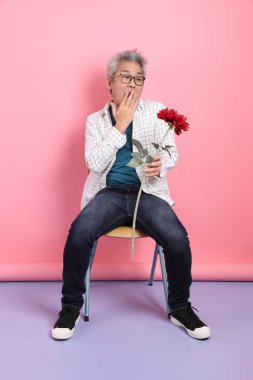 Pembe arka planda izole bir çiçek buketi tutarken sandalyede oturma jesti yapan Asyalı son sınıf öğrencisi. Sevgililer Günü