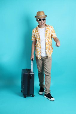 Mavi arka planda, elinde güneş gözlüğü olan Asyalı enerjik yaşlı bir adam bavulu tek başına tutuyor. Olgun adam, Asyalı adam. Yaşlı, stüdyo fotoğrafı. Çoklu duygular. Seyahat kavramı