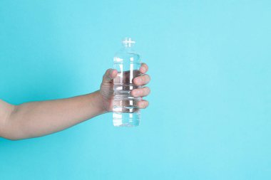 Asyalı bir adamın elinde mavi arka planda izole edilmiş bir şişe su ya da şeffaf plastik şişe bulunur. Beyaz başlık, kapat.. 