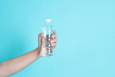 Asyalı bir adamın elinde mavi arka planda izole edilmiş bir şişe su ya da şeffaf plastik şişe bulunur. Beyaz başlık, kapat.. 